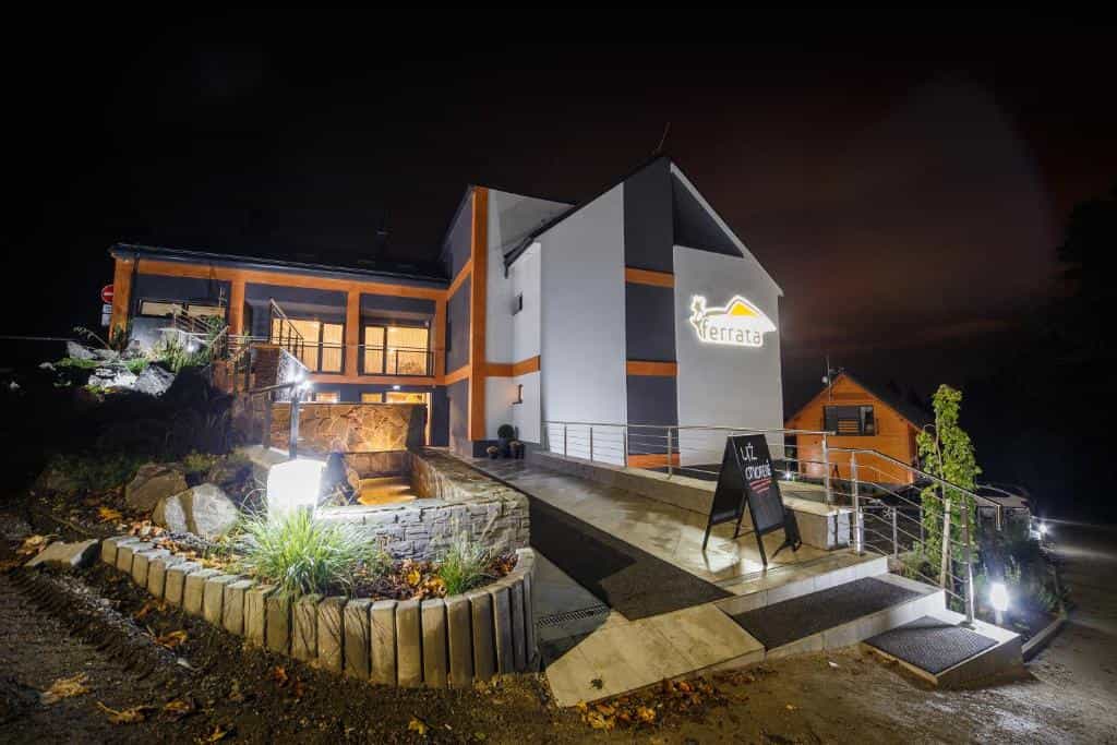 Modern illuminated building entrance at night with "Ferrata" sign and landscaping