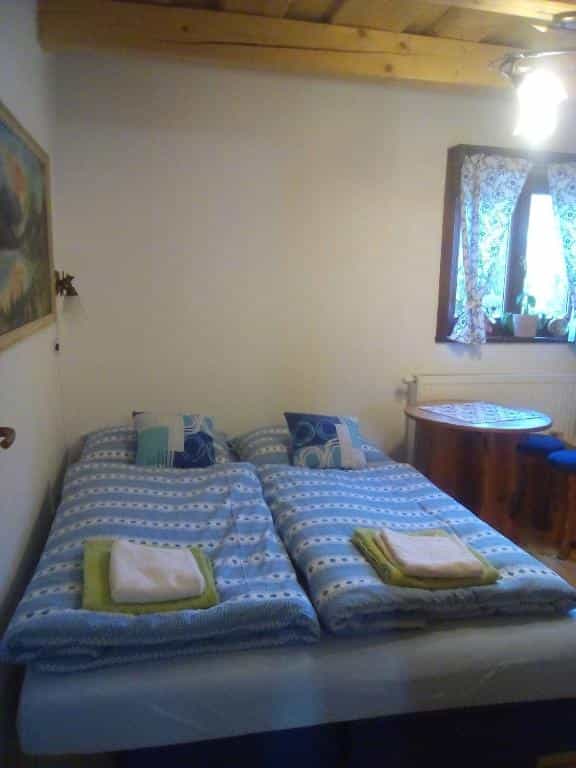 Twin beds with blue striped bedding, wooden ceiling beams, and a window with patterned curtains.
