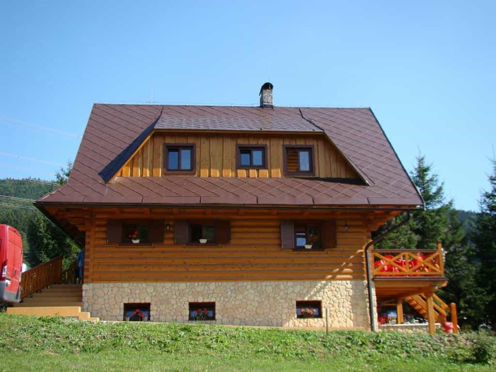 Log cabin recreation house with stone foundation and wooden balcony near forested mountains