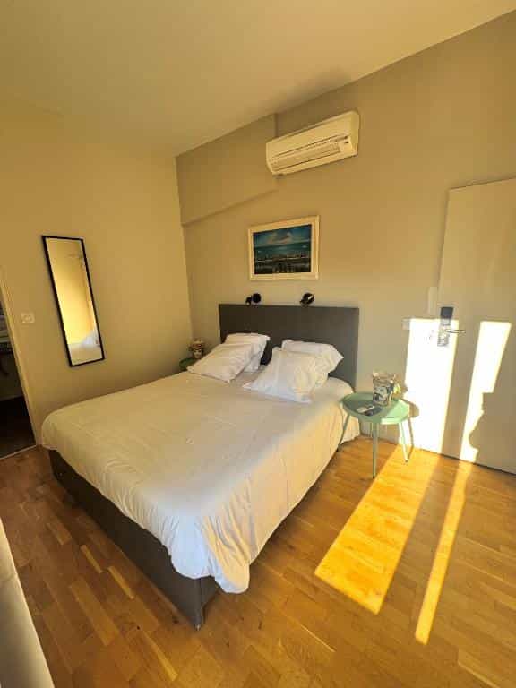 Hotel bedroom with white bedding, wood floor, and sunlight streaming across the room.
