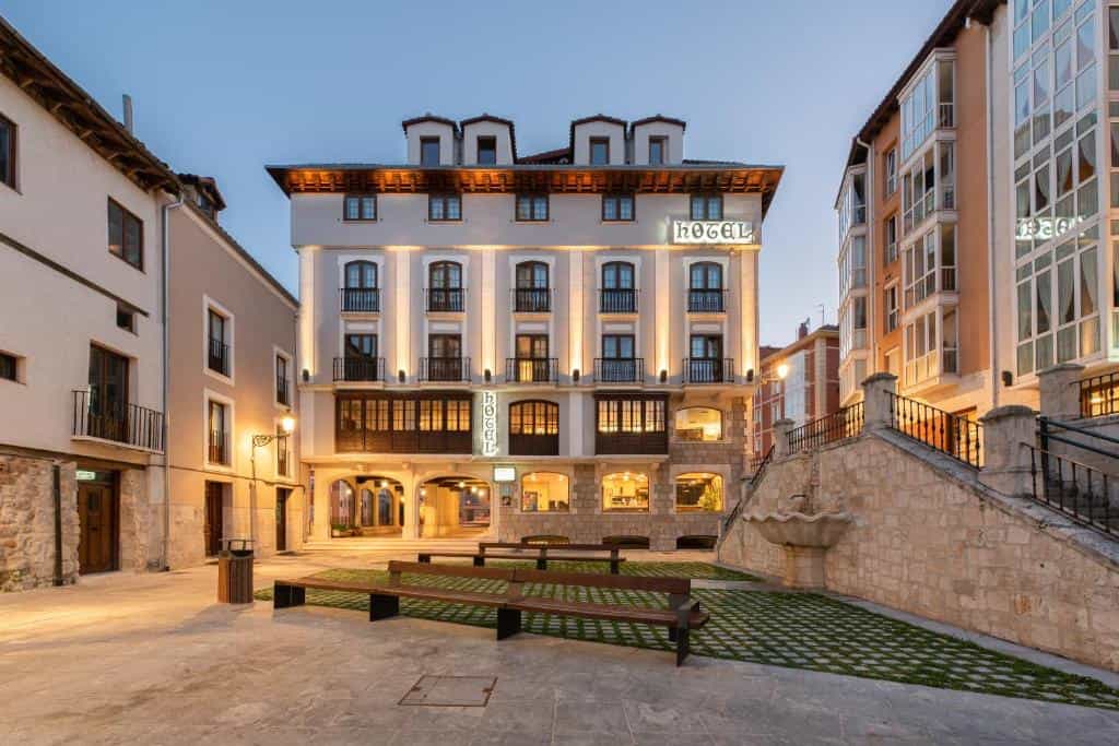 Hotel building illuminated at dusk in a town square with stone fountain and benches.