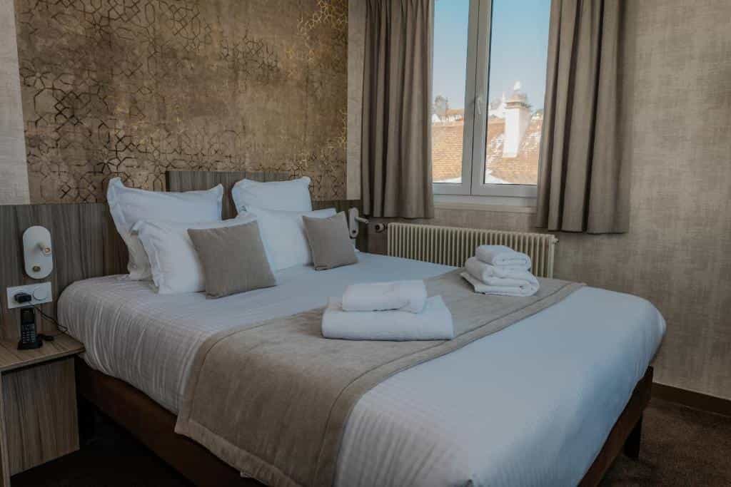 Hotel room with large bed, white linens, and patterned accent wall, view of rooftops outside window.