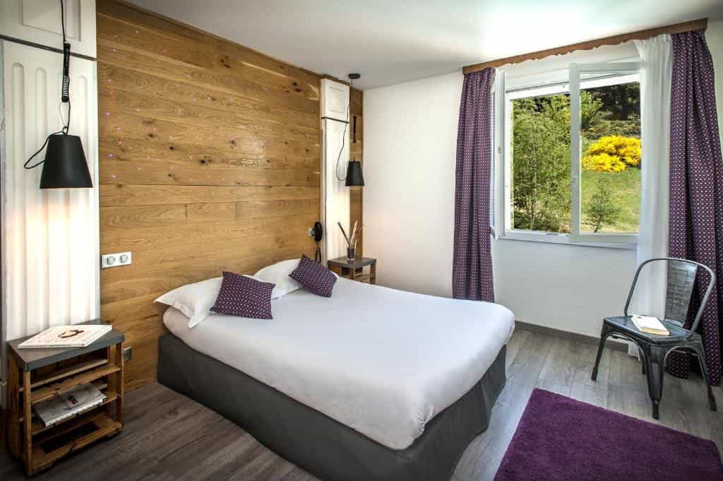 Bedroom with wood accent wall, white bedding, and window view of green hillside.
