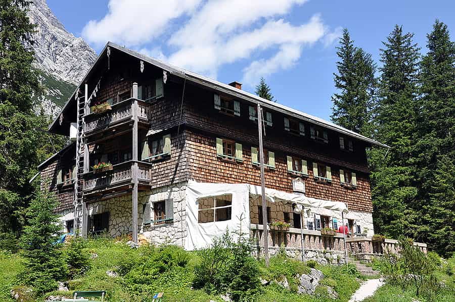 Reintalangerhütte mountain hut with wooden balconies surrounded by pine forest and rocky peaks.
