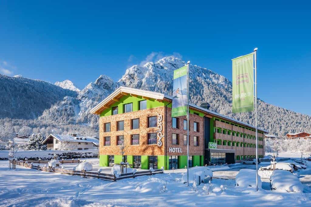 Explorer Hotel Berchtesgaden in winter with snow-covered mountains and bright blue sky.