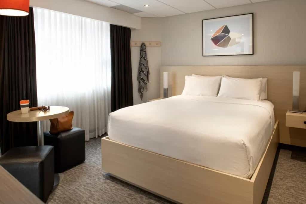 Modern hotel room with white bedding, light wood accents, and a window with dark curtains in Banff Aspen Lodge.