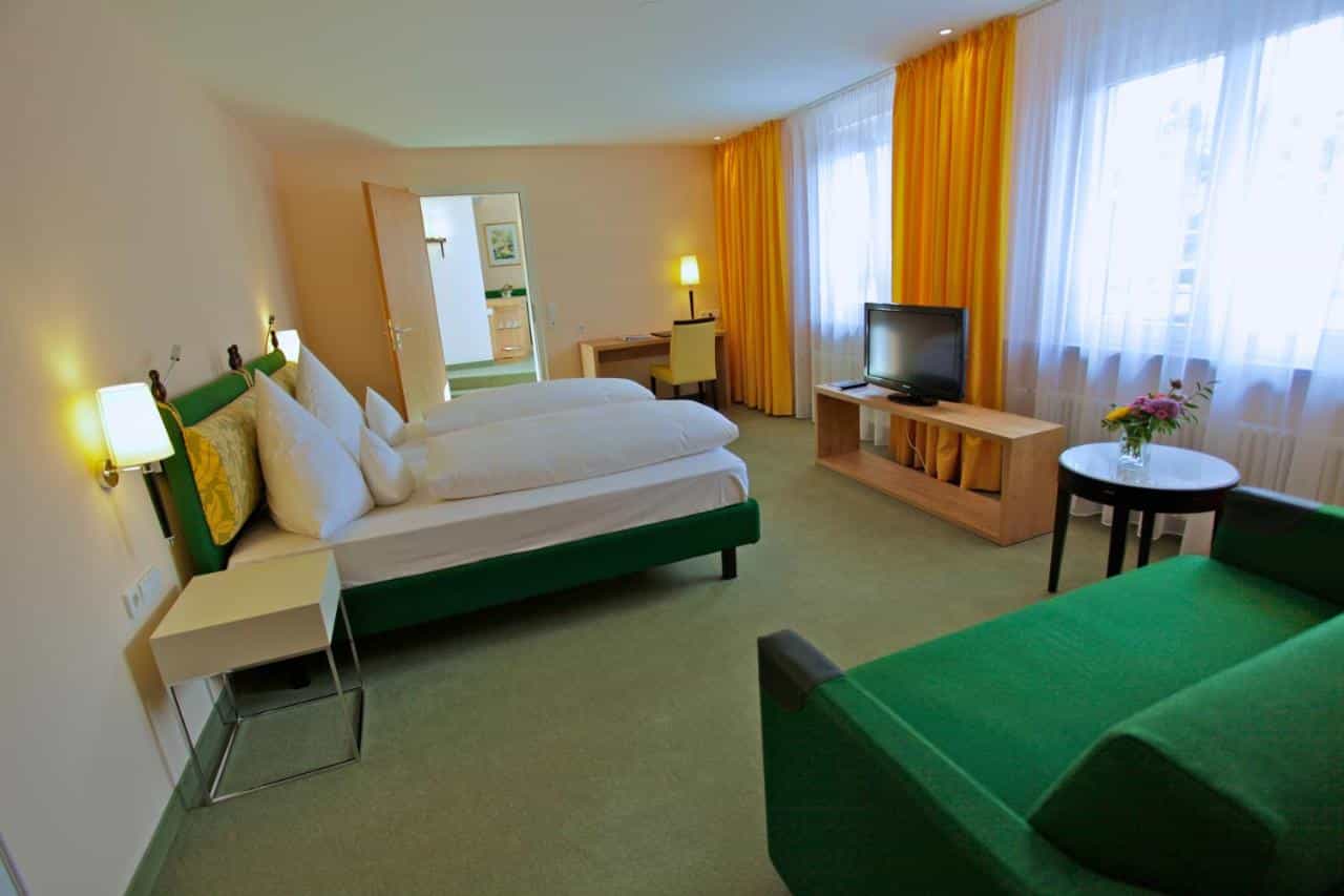 Parkhotel Flora am Schluchsee room with green bed and yellow curtains.
