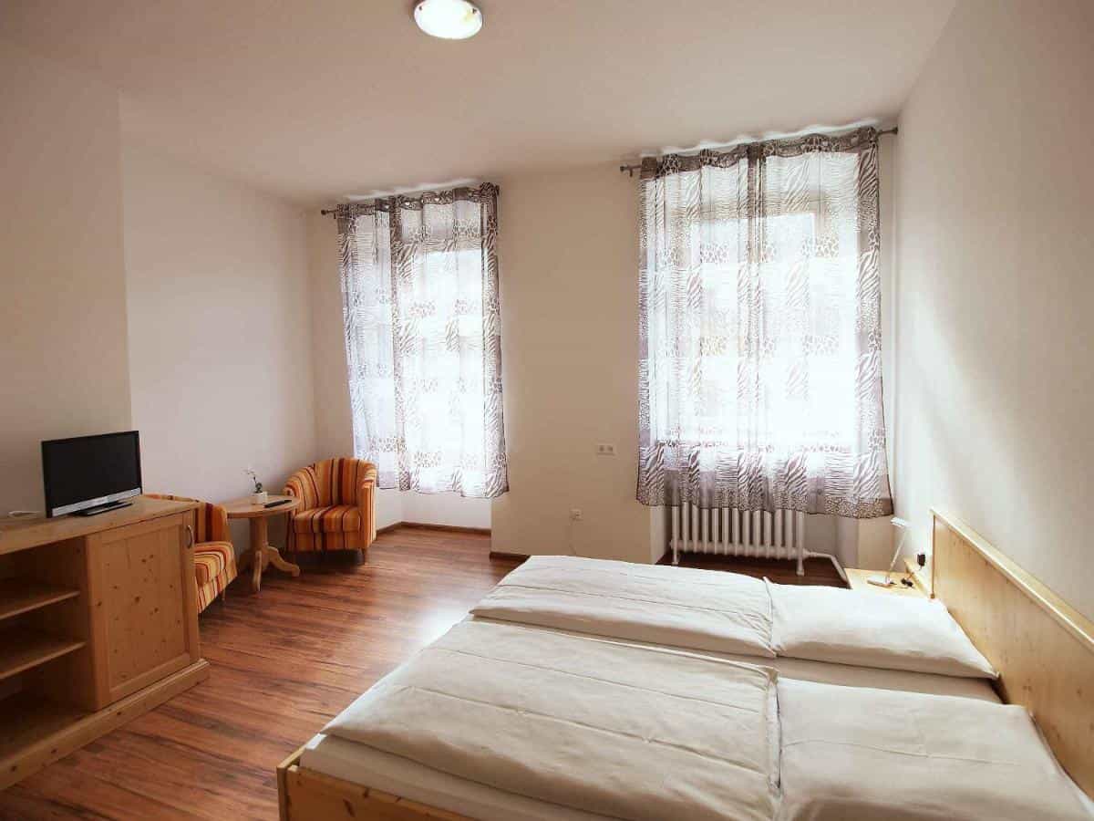 Hotel Klosterhof twin room with wood furniture, striped armchairs, and sheer patterned curtains.