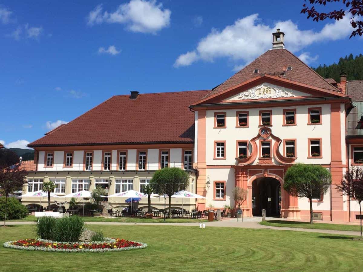 Hotel Klosterhof building with red roof, white facade, and outdoor dining area on sunny day.