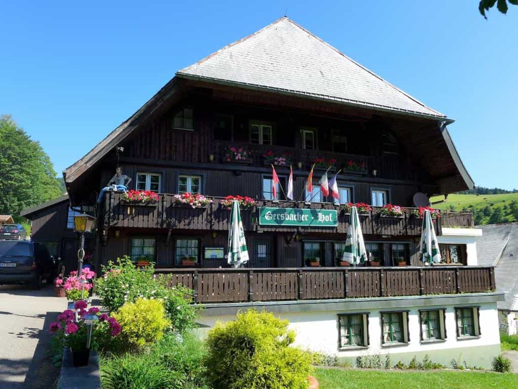 Genusshotel Gersbacher Hof building with dark wood facade, flower boxes, and green hills in background.