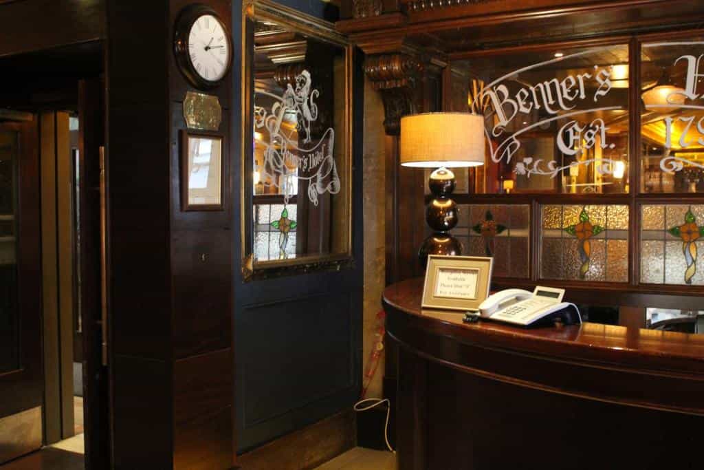 Hotel reception desk with dark wood, lamp, phone, and "Benners Hotel" etched glass.