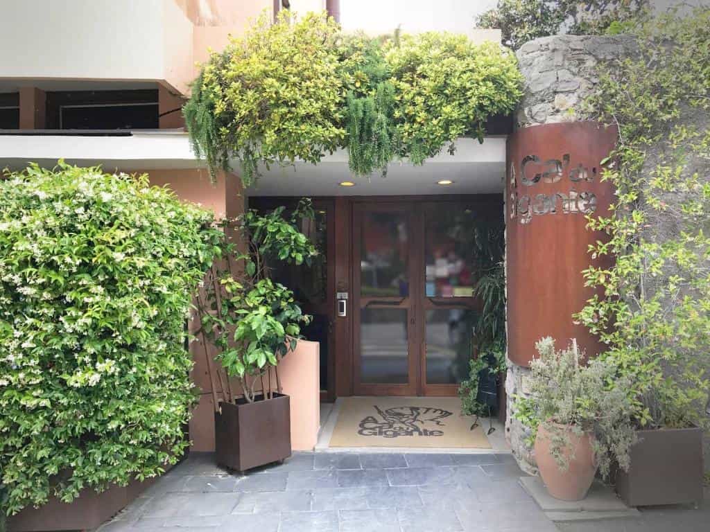 Entrance to Locanda A Cà Du Gigante with lush greenery, wood doors, and rusted metal signage.
