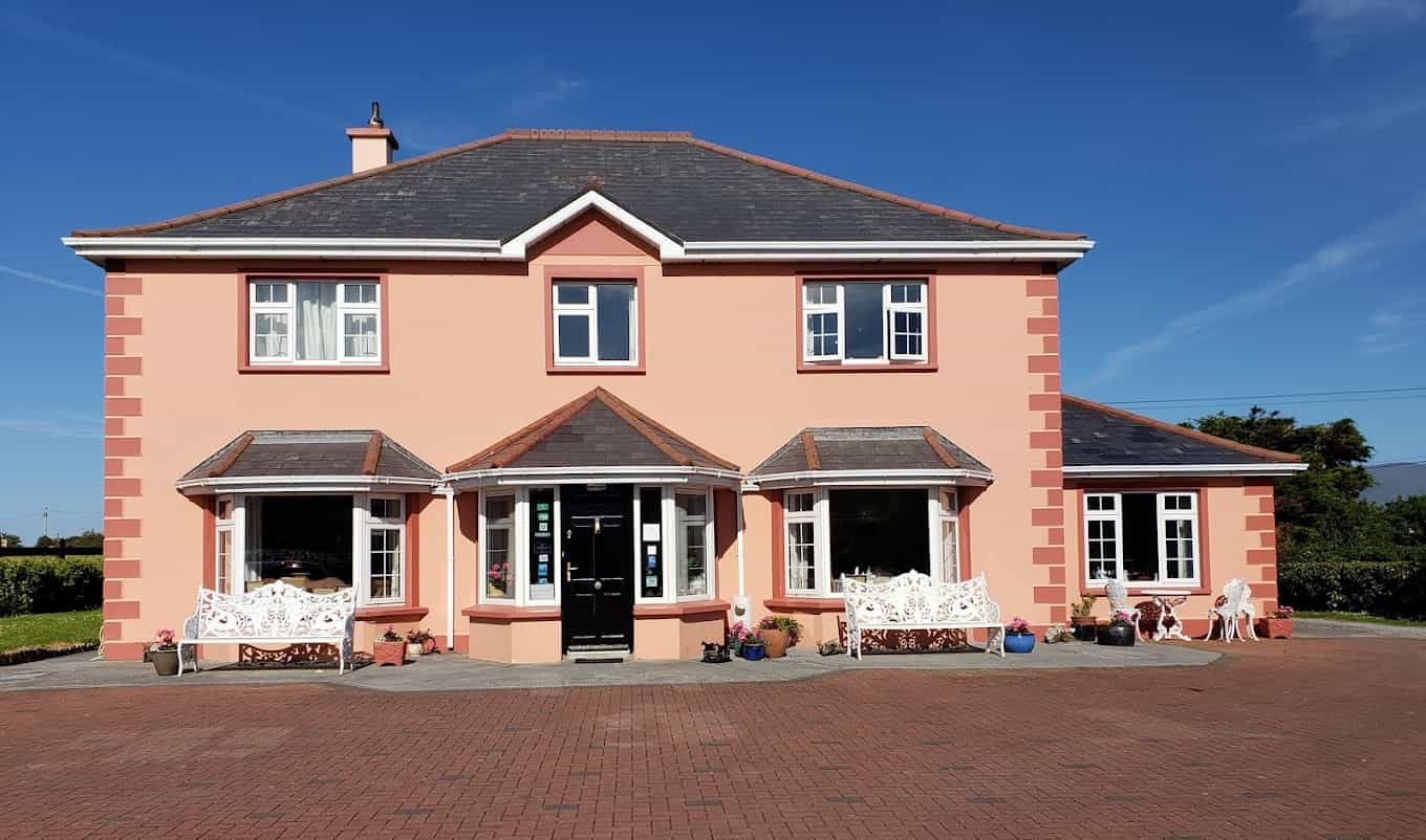 Peach-colored bed and breakfast house with white trim, bay windows, and white iron benches under blue sky.