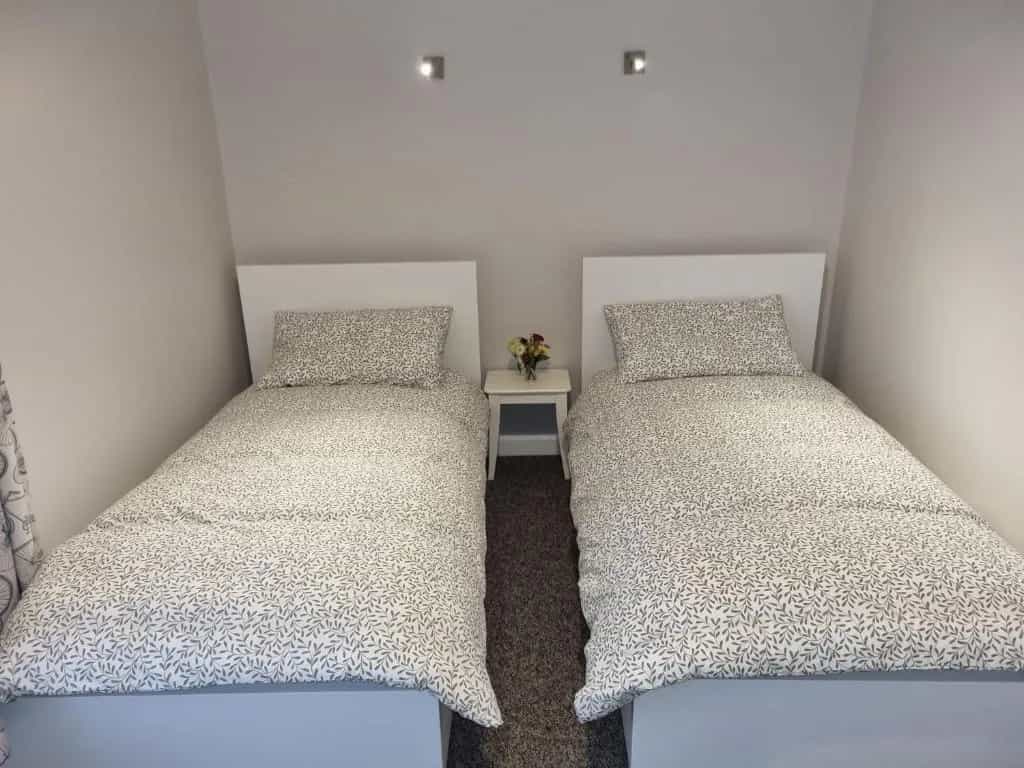 Twin beds with white headboards and gray leaf-patterned bedding in a small room.