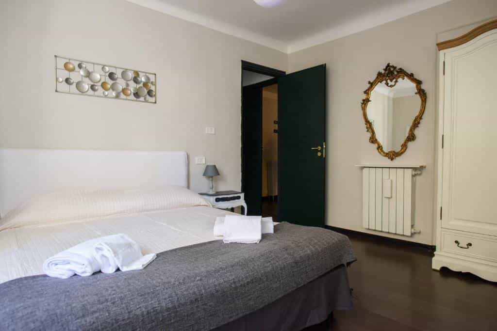 Bedroom with white bedding, dark wood floor, ornate mirror, and open dark green door.