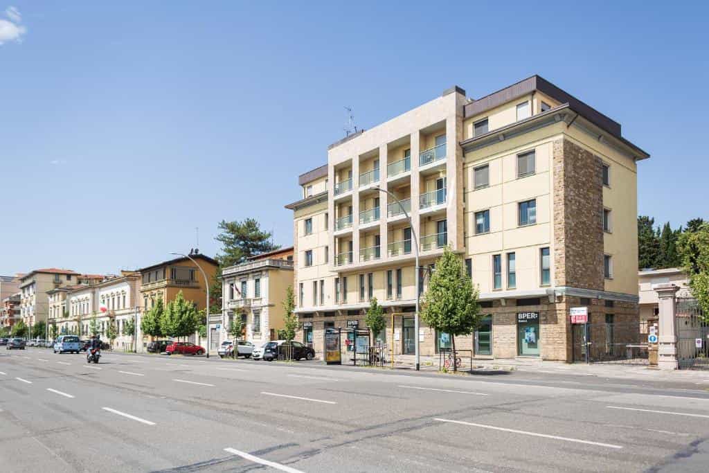 Apartment building facade along a wide city street with parked cars and clear blue sky.
