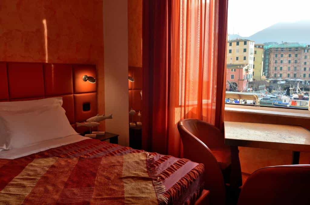 Hotel room with orange decor overlooking harbor with boats and colorful buildings