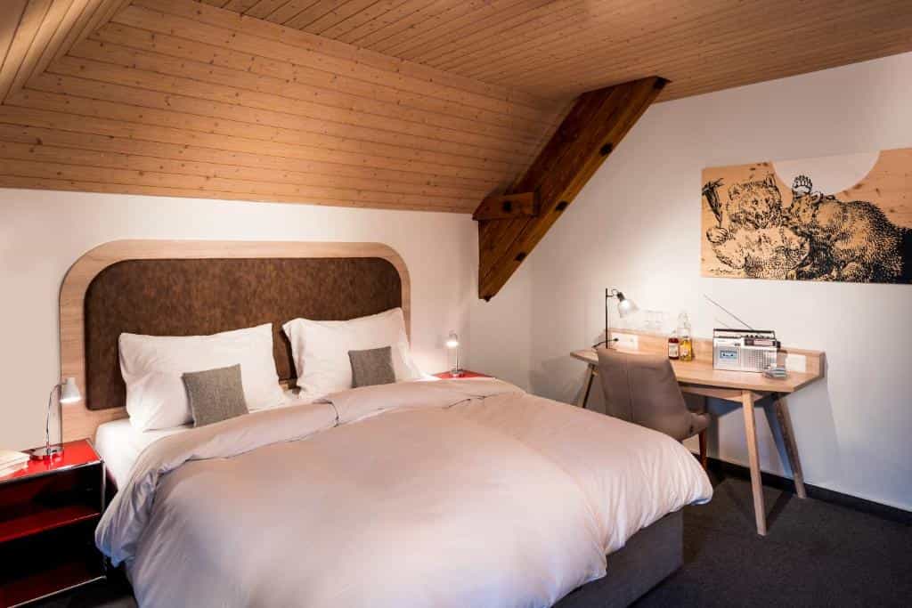 Hotel room with wood-paneled ceiling, large bed, and desk with bear artwork.