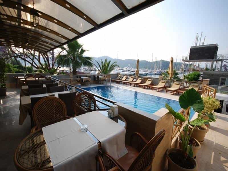 Outdoor dining area with wicker chairs next to a pool overlooking a marina with many sailboats.