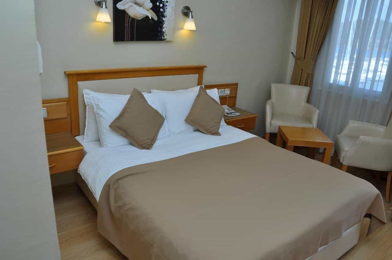 Hotel Doruk room with wooden headboard, white linens, beige accents, and sheer curtains.