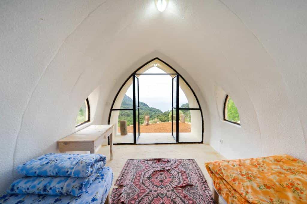 Interior of white dome room with arched door opening to green mountainside view