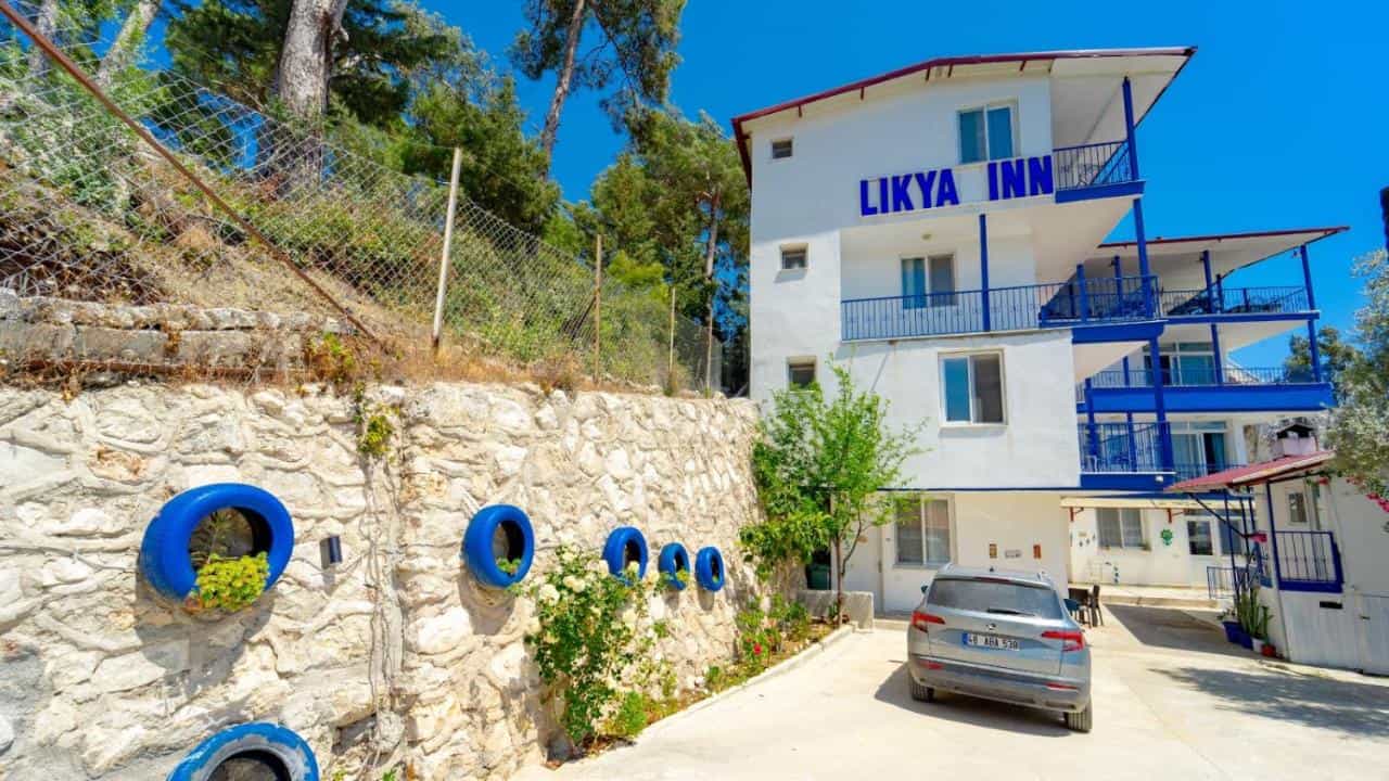 Likya Inn white building with blue balconies next to stone retaining wall with tire planters.