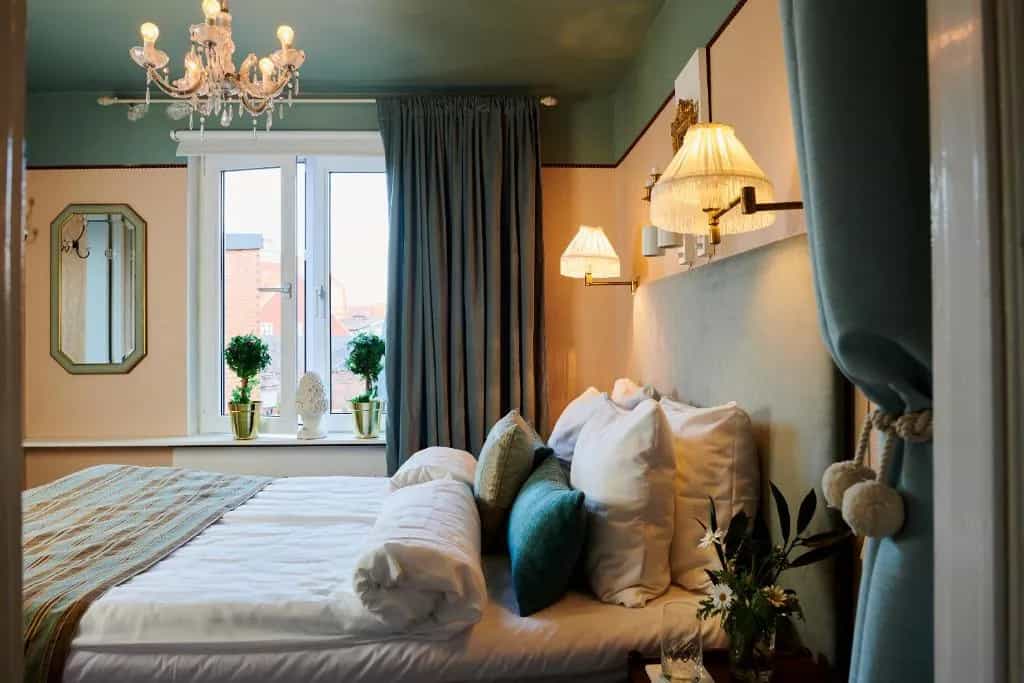 Hotel room at Hotell Bäckagården with chandelier, window, and plush bedding.