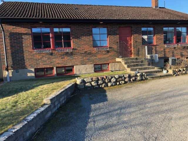 Brick house with red window frames, stone retaining wall, and gravel driveway in Österlen, Skillinge.