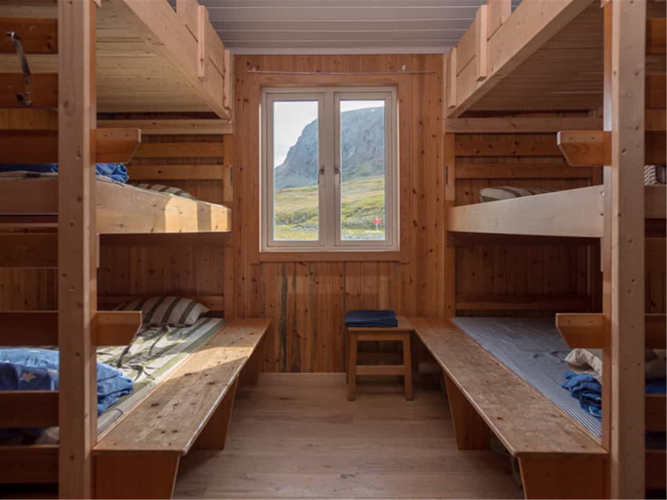 Wooden bunk room interior with window view of grassy mountain landscape