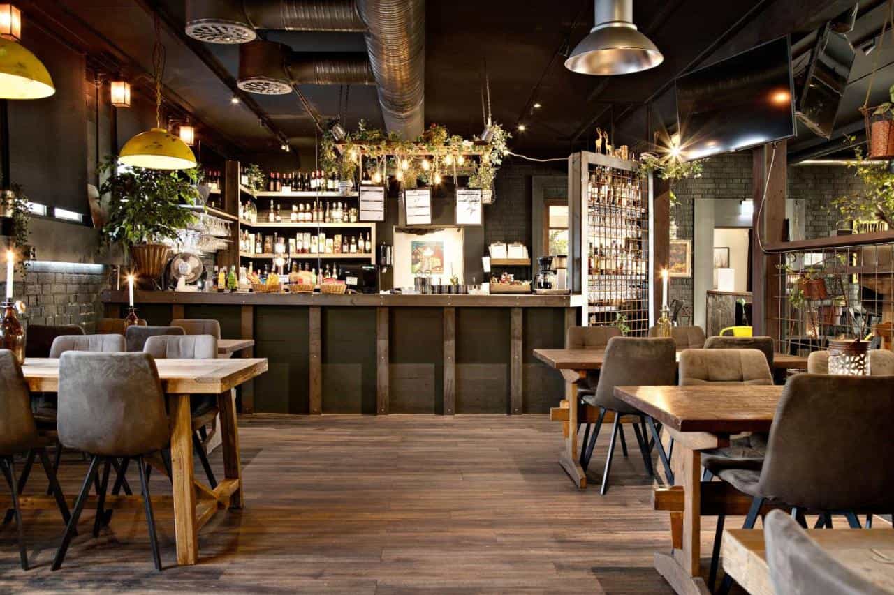 Interior of a dimly lit bar or restaurant with wooden tables, gray chairs, and a well-stocked bar area.