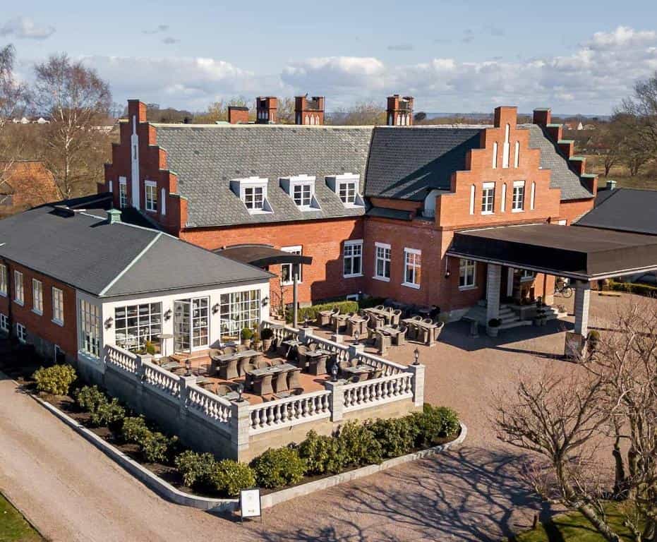 Brick hotel building with outdoor terrace seating and covered entrance drive, Villa Brunnby.