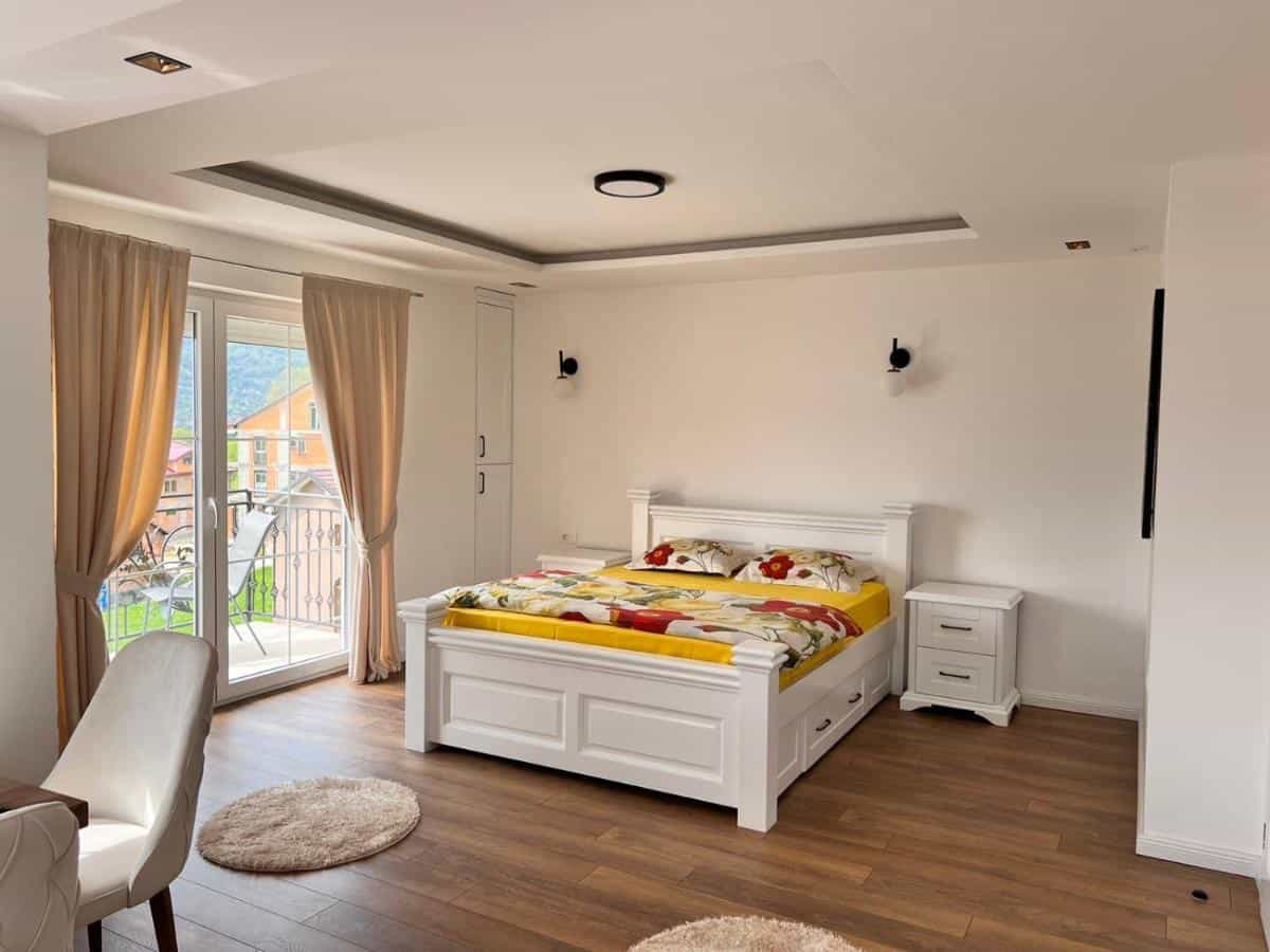 Bright bedroom with white furniture, wood floor, and balcony view of green mountains.