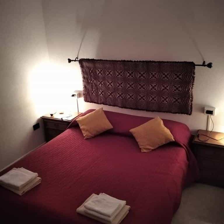 Bedroom with red bedding, yellow pillows, and woven tapestry headboard in San Francesco B&B