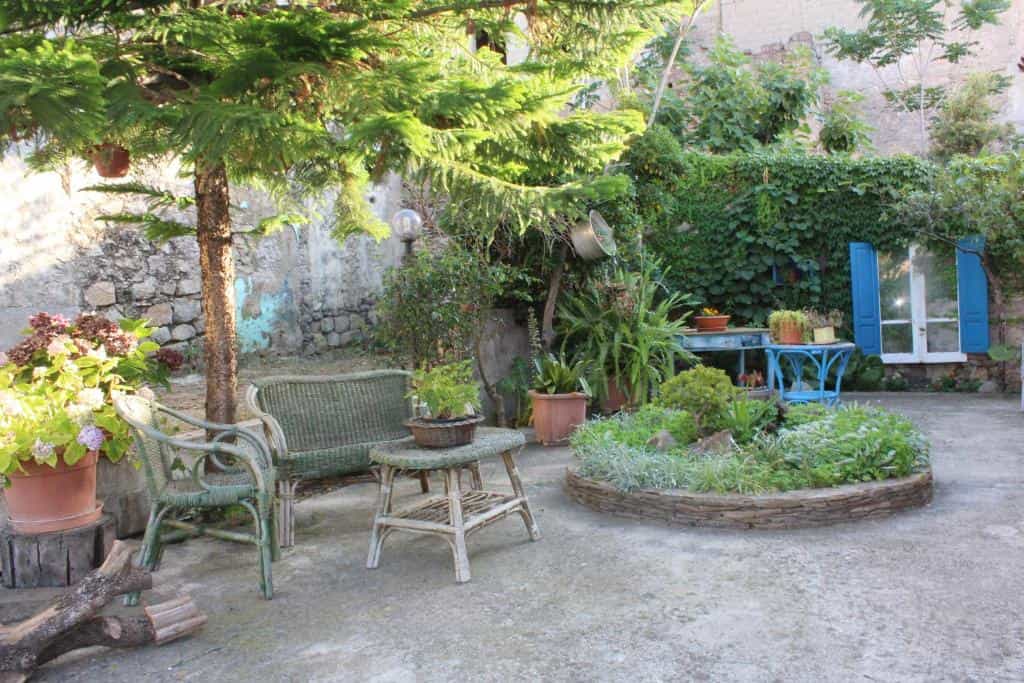 Lush garden patio with wicker furniture, potted plants, and stone planter near San Francesco.