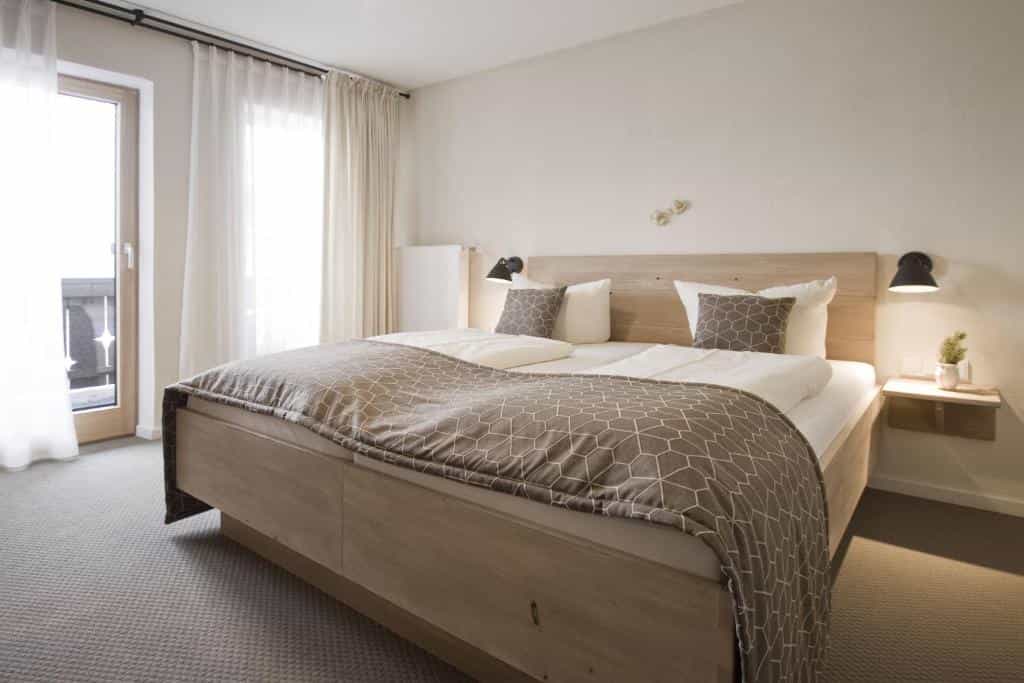 Bright hotel room with large wooden bed, geometric brown blanket, and balcony door in Bavaria.