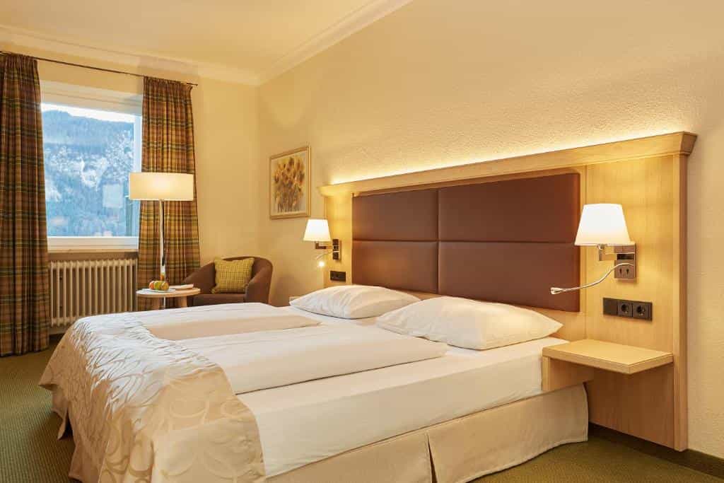 Hotel room with twin beds, wood headboard, and view of snowy mountains outside window.