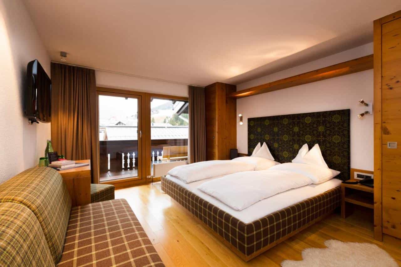 Hotel Sandhof room with wood accents, plaid sofa, and balcony view of a village.