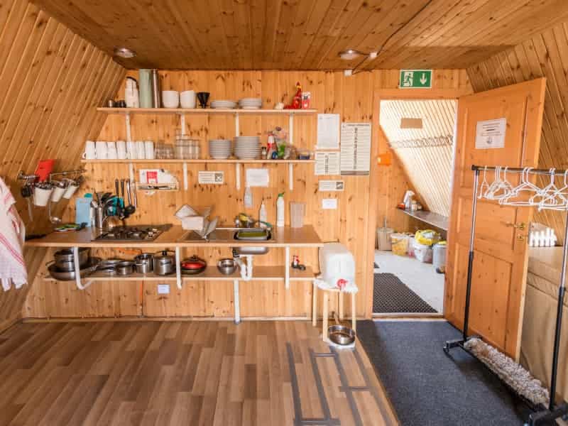 Self-catering kitchen with wooden walls, shelves of dishes, and cooking gear in Fimmvörðuháls hut.