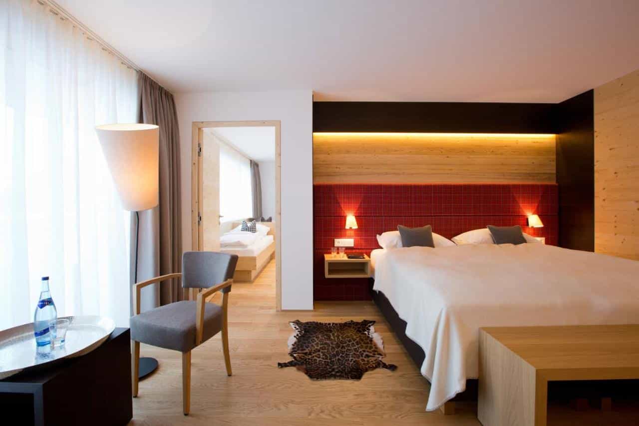 Hotel Walserstube room with wooden accents, red headboard, and view into a second bedroom.