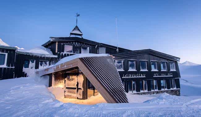 Leirvassbu mountain lodge heavily covered in snow under a clear blue winter sky.