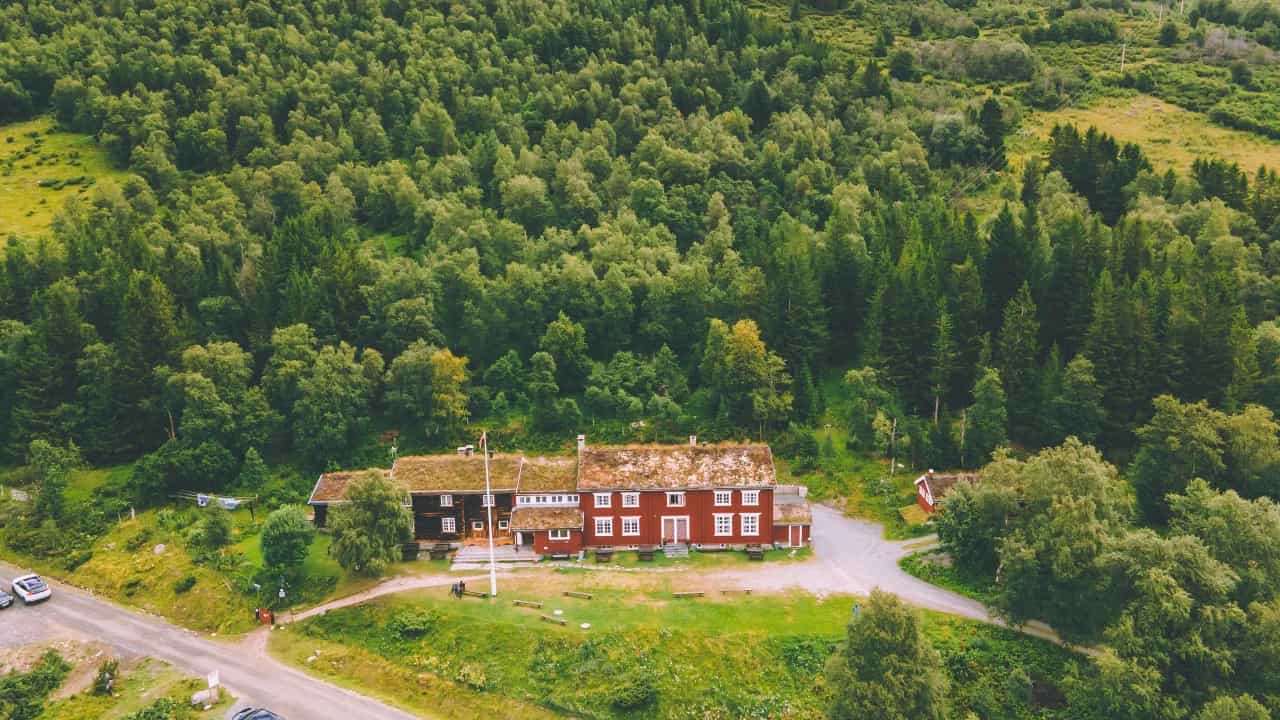 Gjevillvasshytta cabin with grass roof nestled in dense green forest and mountains.