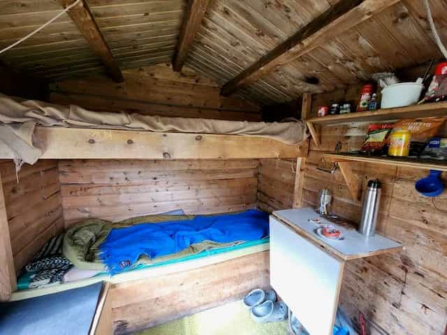 Interior of rustic wooden hut with bunk beds, sleeping bag, and small fold-down table, Trollheimshytta.