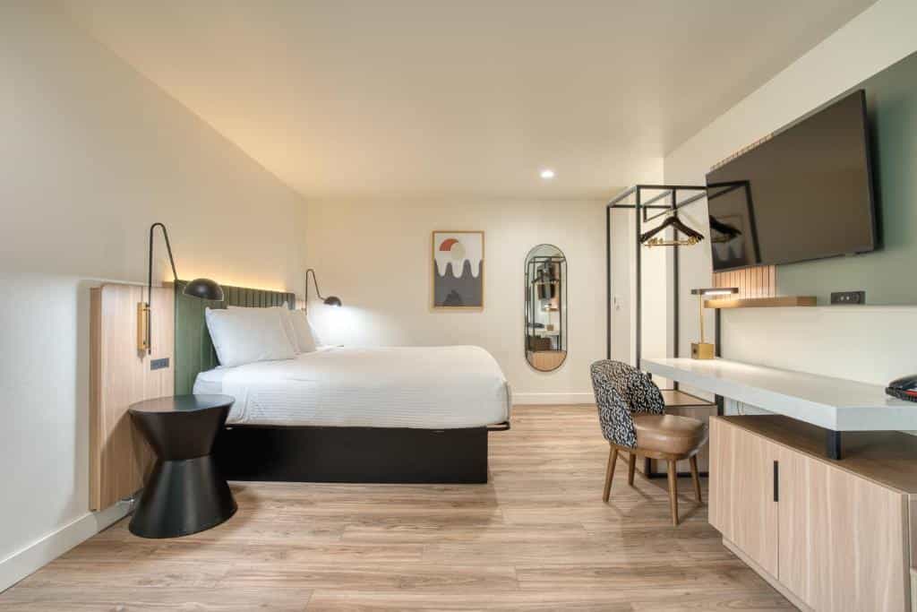 Modern hotel room with white bedding, wood floors, and a mounted television.