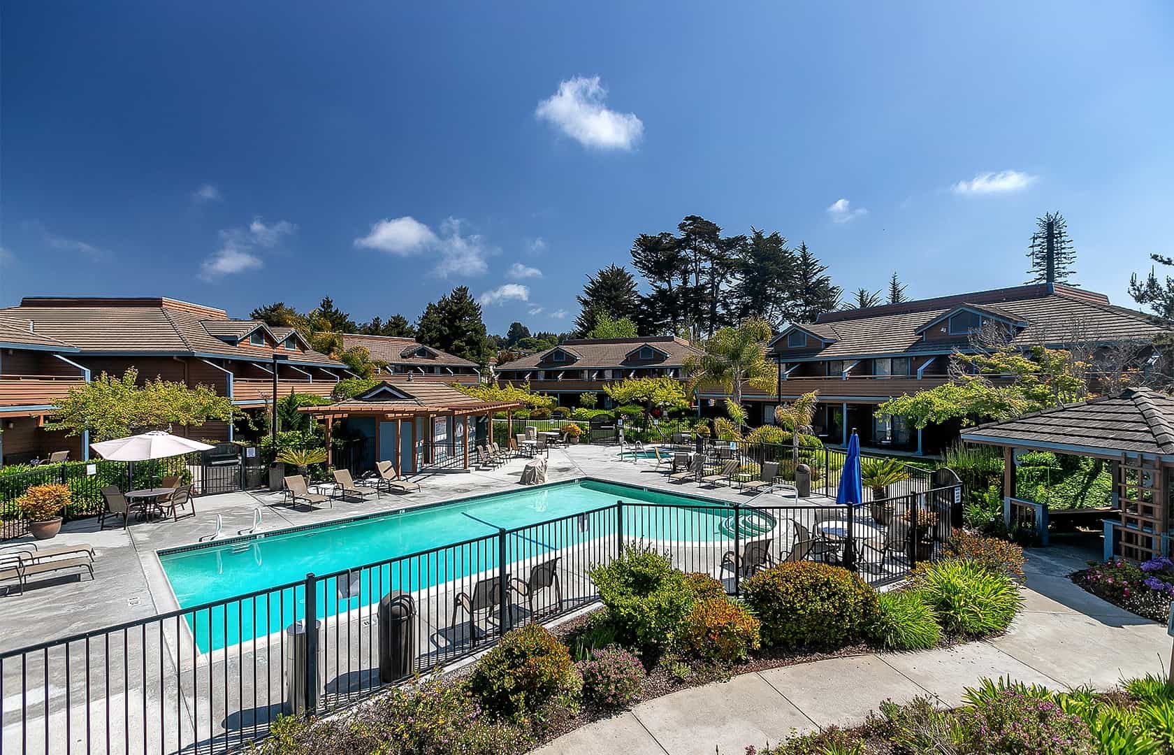 Swimming pool area with lounge chairs surrounded by brown-roofed buildings at Seacliff Inn Aptos.