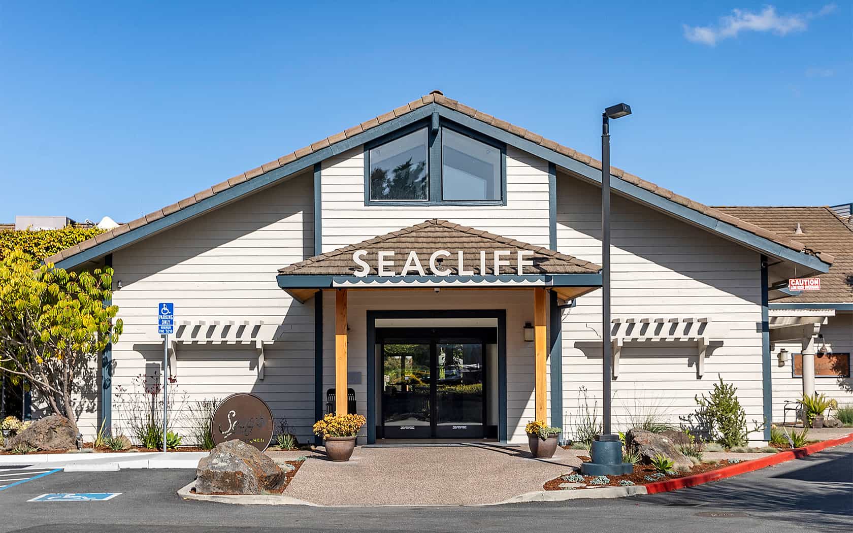 Seacliff Inn entrance in Aptos with light siding, brown roof, and blue sky.