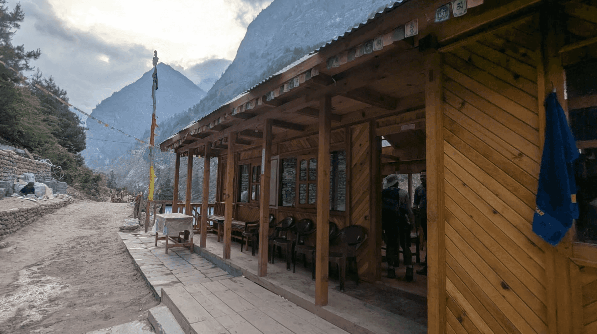 Wooden Ghap Cottage guest house porch with prayer flags against steep mountainside.