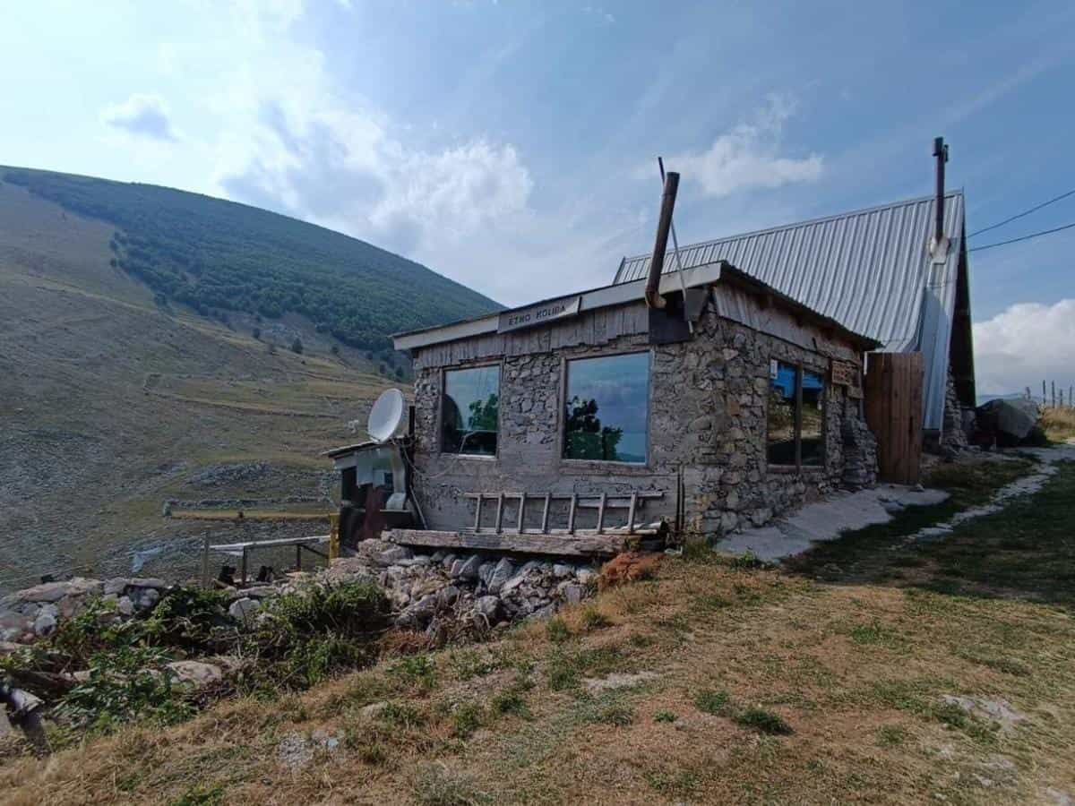 Stone Etno-Koliba Bed & Breakfast nestled on grassy hillside below large mountain slope