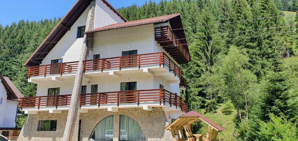 Guesthouse Alegria with white walls and wooden balconies against a dense green forest backdrop.