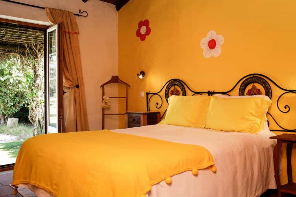 Bedroom with yellow walls, wrought iron bed frame, and open glass doors leading to a garden.