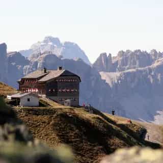 Sillianer Hütte mountain hut on a grassy ridge with rocky Dolomite peaks in the background.
